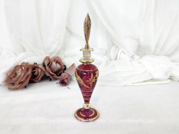 Sur 17 cm de haut, voici une fiole en verre soufflé décorée de dorures en relief en forme d'amphore couleur bordeaux avec un grand bouchon en forme de feuille dorée .